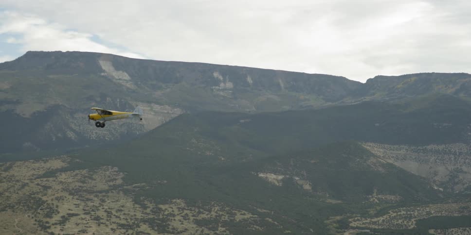 A small, single-engine plane flies over a mountain range