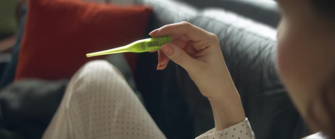 A person pulls a thermometer from their underarm and looks at the reading