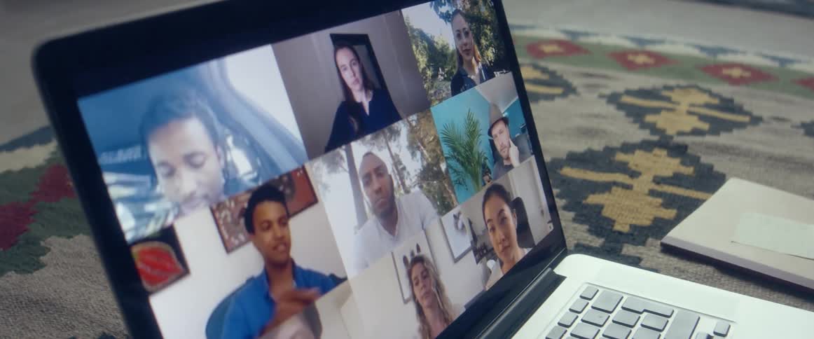 A group of friends having a meeting through a video call on a laptop over a rug in the living room