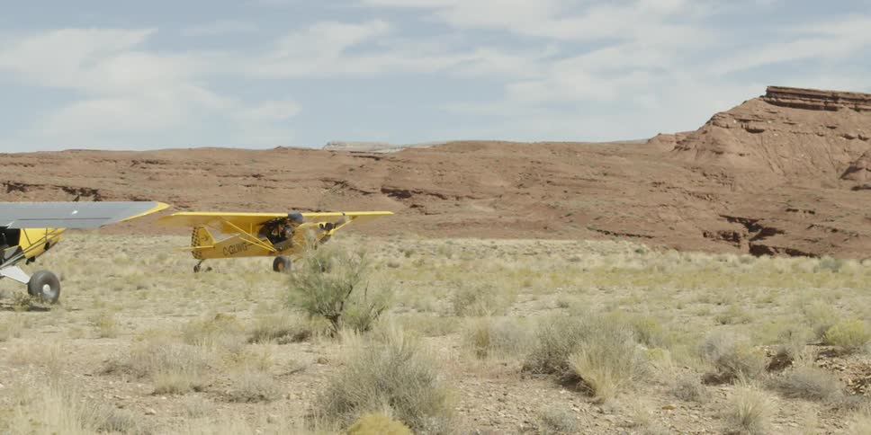 A small yellow single engine plane landing on a dirt runway in the desert