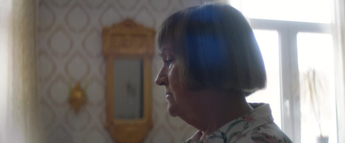 Woman with short bobbed hair stands in home near curtained windows