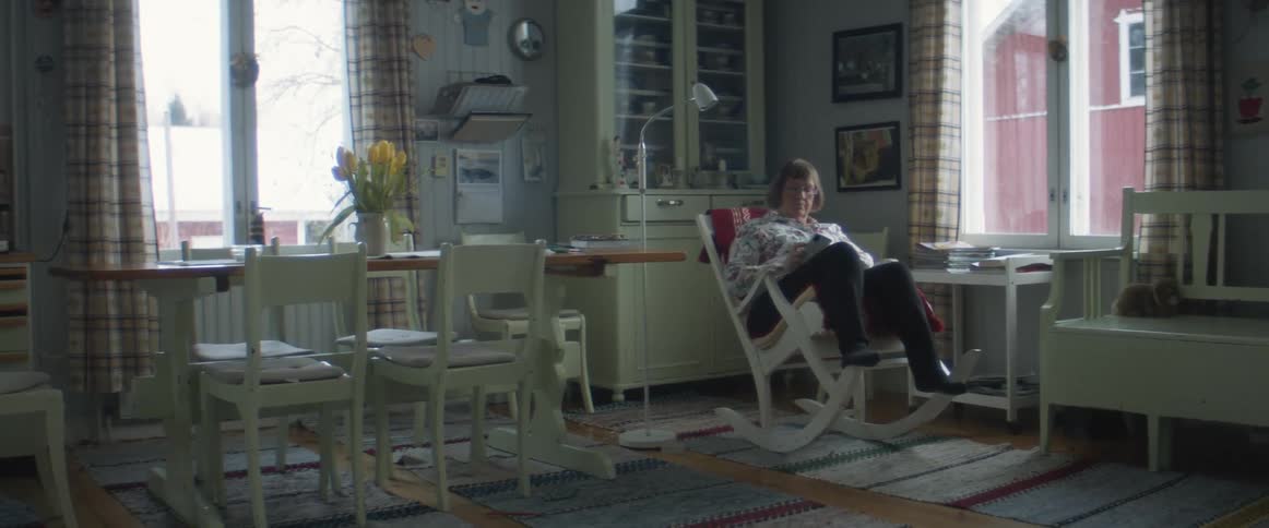 A woman in a room sitting in a rocking chair next to a table and chairs