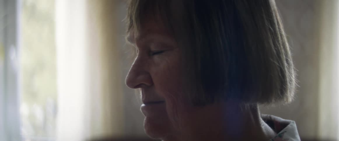 A woman in a room smiling with a wall and window in the background
