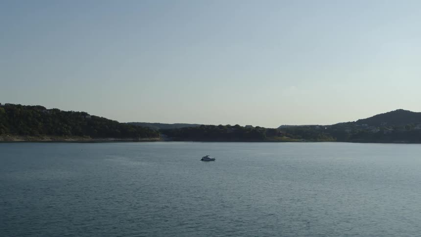 A boat on a lake with land the sky and clouds in the background