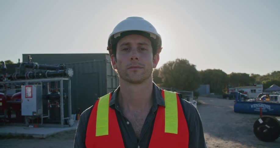 A construction worker with a helmet and safety vest on walks through a lot
