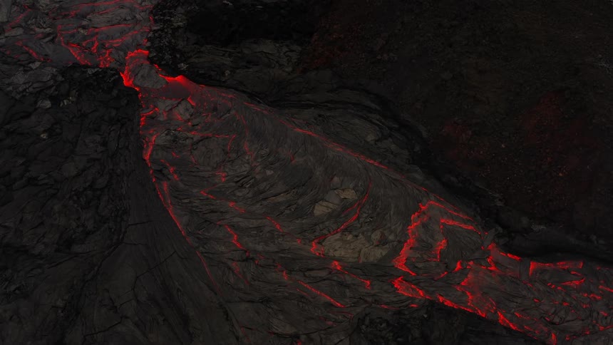 River of molten hot lava moves slowly as it glows in the darkness