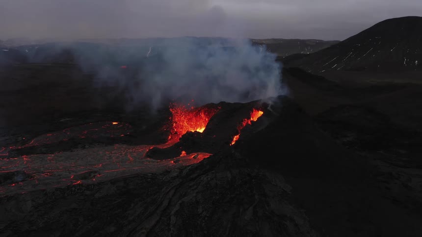Smoke rises as a volcano erupts and spews molten hot lava