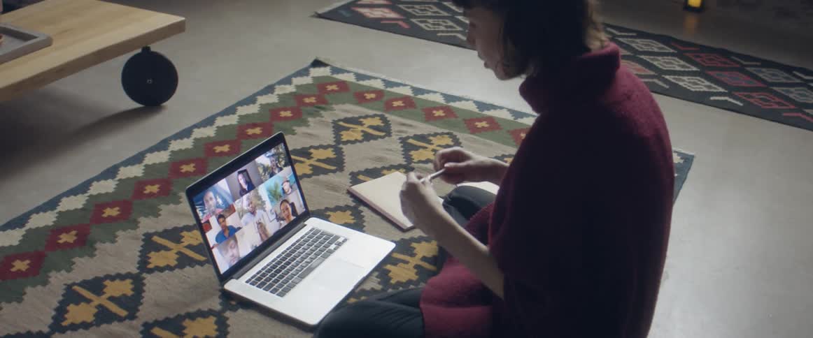Woman sitting over a rug in the living room talking to a group of friends through a video call on a laptop