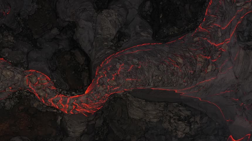 River of molten hot lava moves slowly as it glows in the darkness