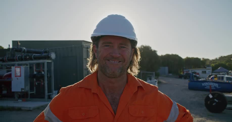 A man in a hardhat standing and staring with trees the sky and clouds in the background