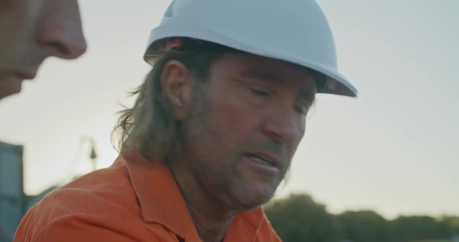 Construction workers checking blueprints on a laptop in the worksite at sunset