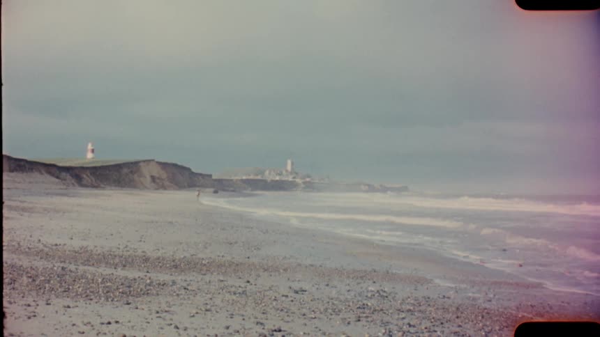 Waves roll in on a beach and a lighthouse is in the distance on analog Film 16mm