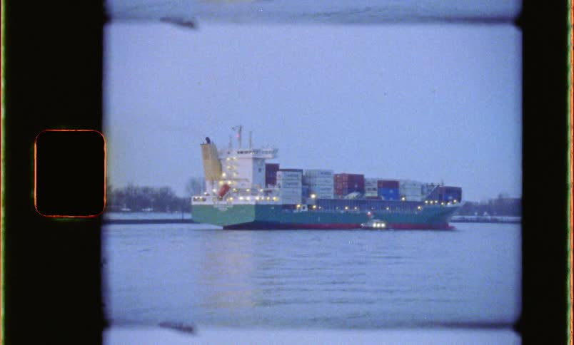 A freighter cargo container ship loaded with intermodal containers on a river caught on vintage film