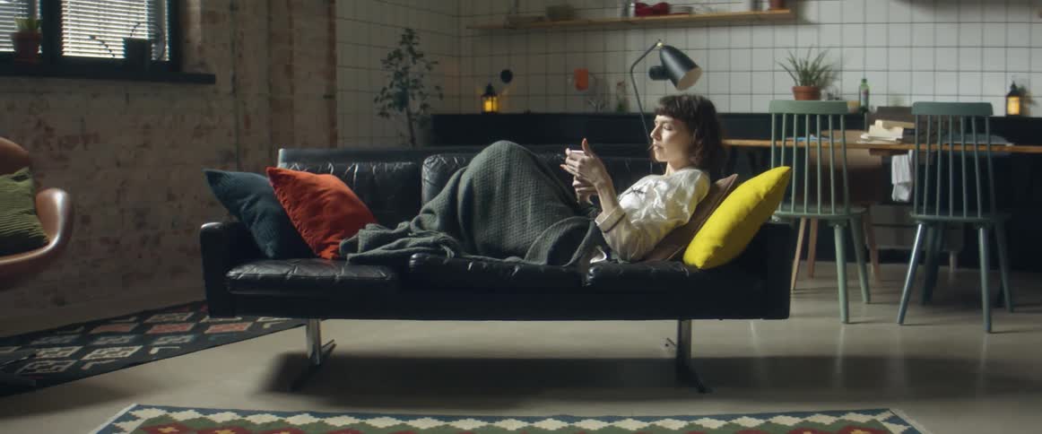 Woman walks into living room to lie down on sofa with mobile phone