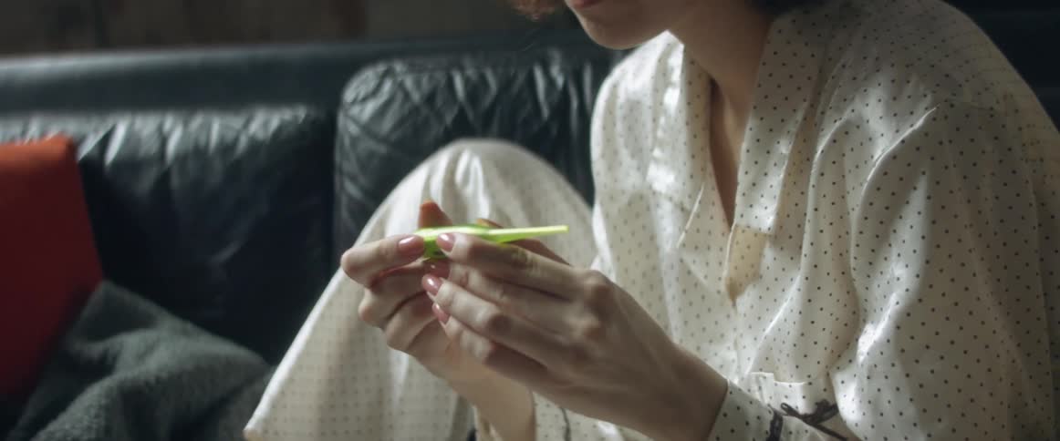 Woman sitting in a couch wearing pajamas at home takes her temperature
