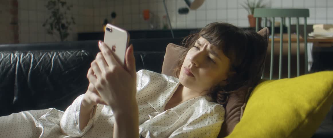 Woman reclined in a couch at home wearing pajamas checking her smartphone