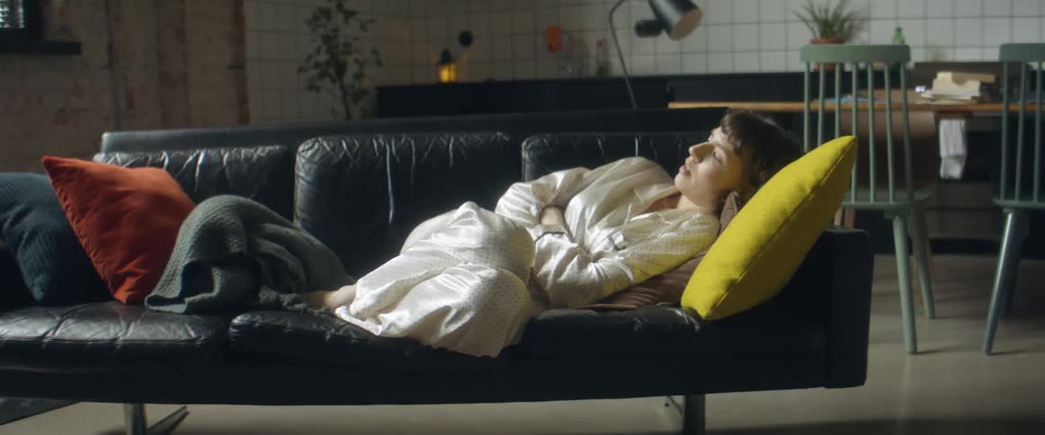 A woman looks at then puts down her phone and lies back on the couch in her pajamas