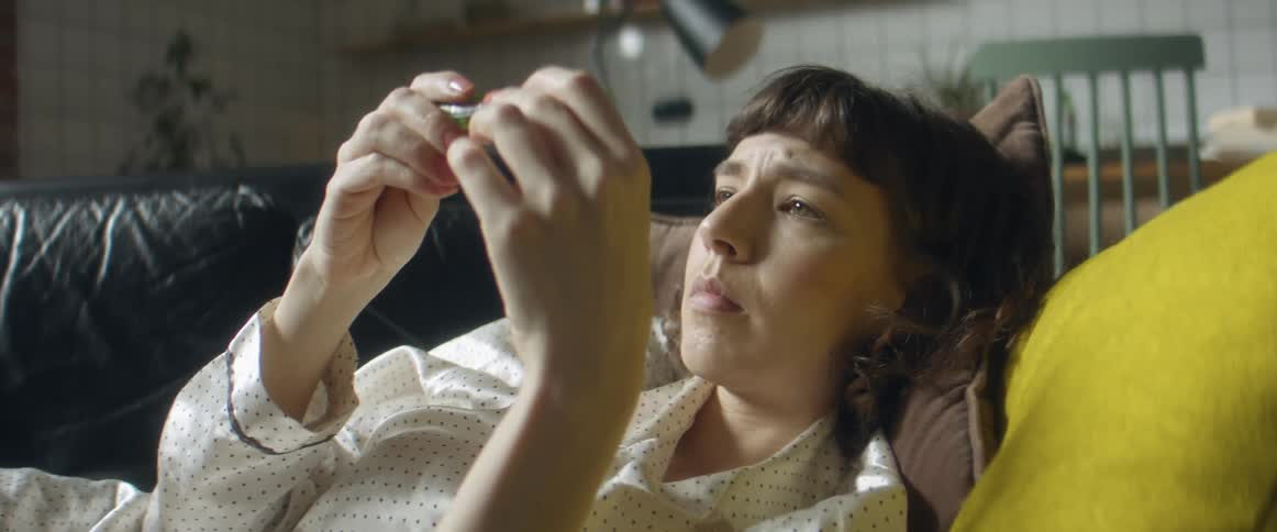 A woman in pajamas laying on a couch with a wall and a chair in the background