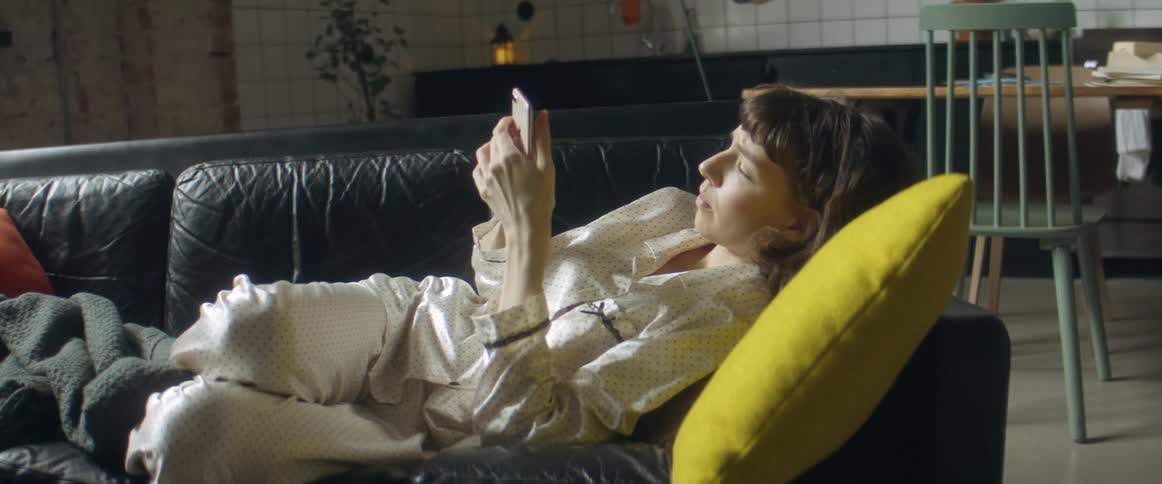 Woman reclined in a couch at home wearing pajamas checking her smartphone