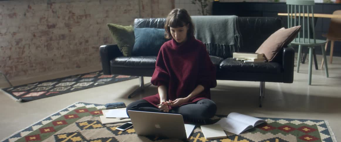 A woman studies on the floor of her living room with her laptop and textbooks around her