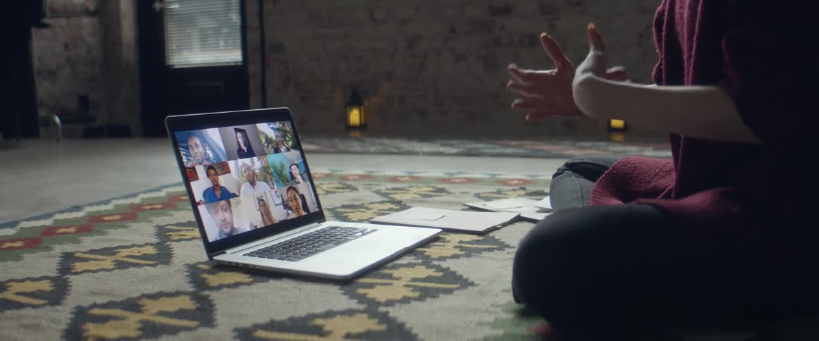 A person in a room sitting on the floor in front of a laptop with a wall and door in the background