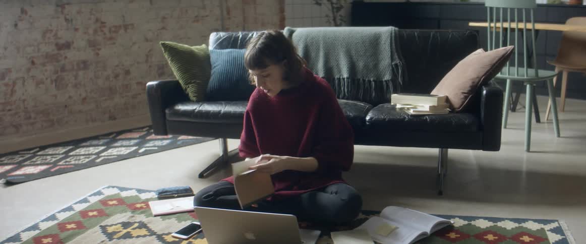 A woman sits on the floor in front of a laptop going through a notebook