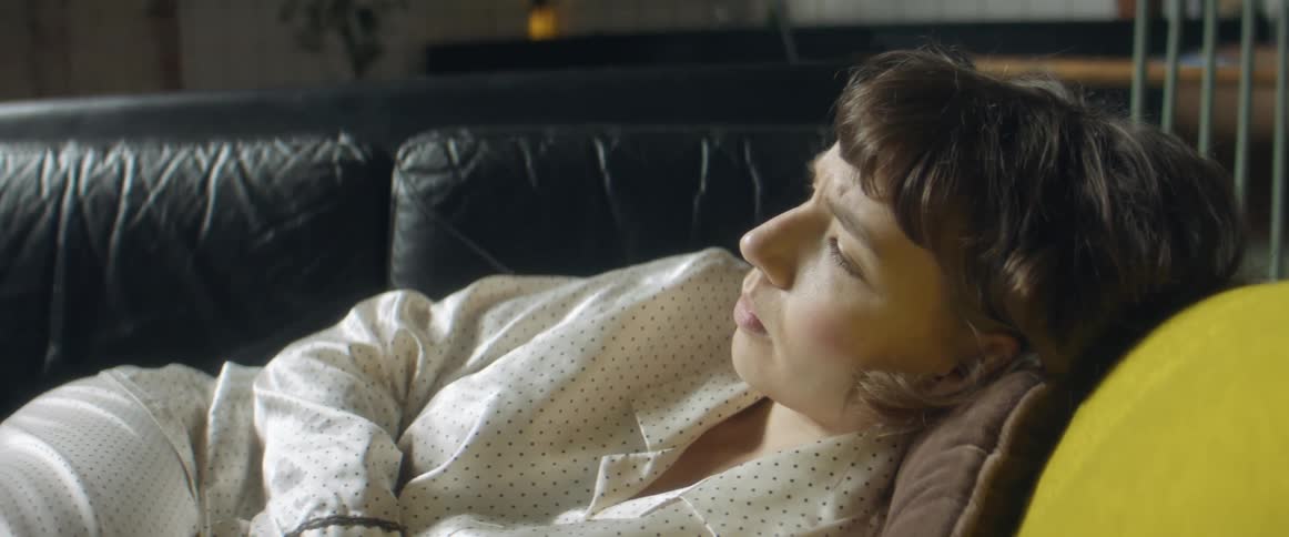 Woman wearing pajamas lies on sofa with arms crossed frowning