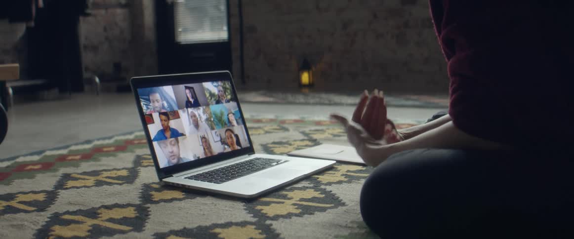 Woman sitting over a rug in the living room talking to a group of friends through a video call on a laptop