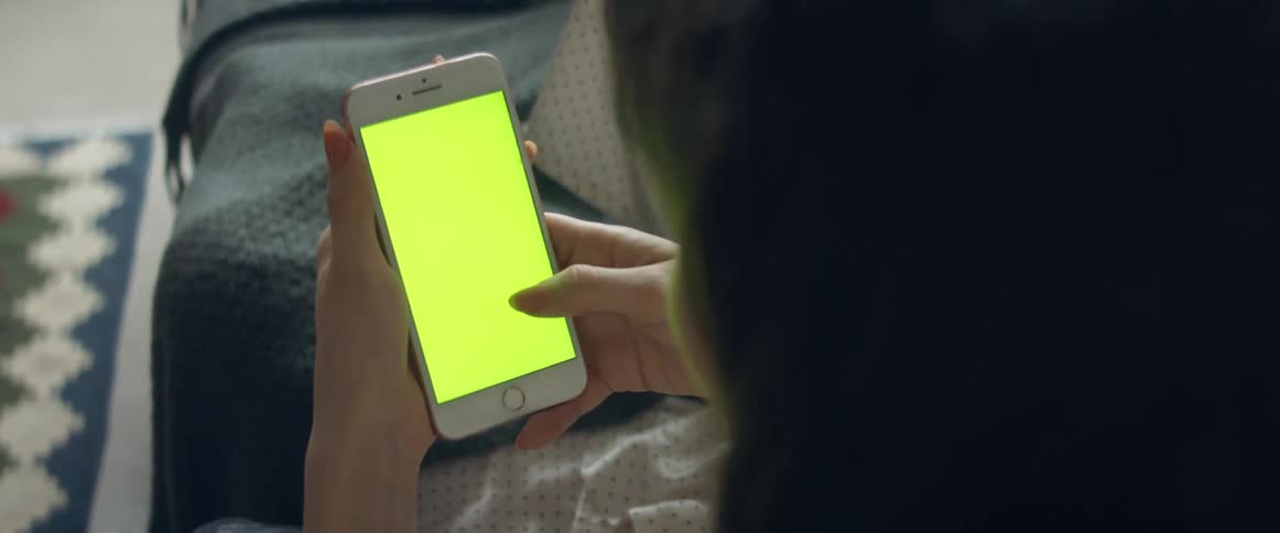A woman lying on a couch scrolling on the screen of an iphone