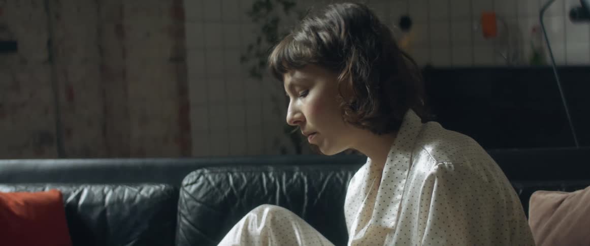 Woman wearing pajamas sitting in a couch at home takes her temperature