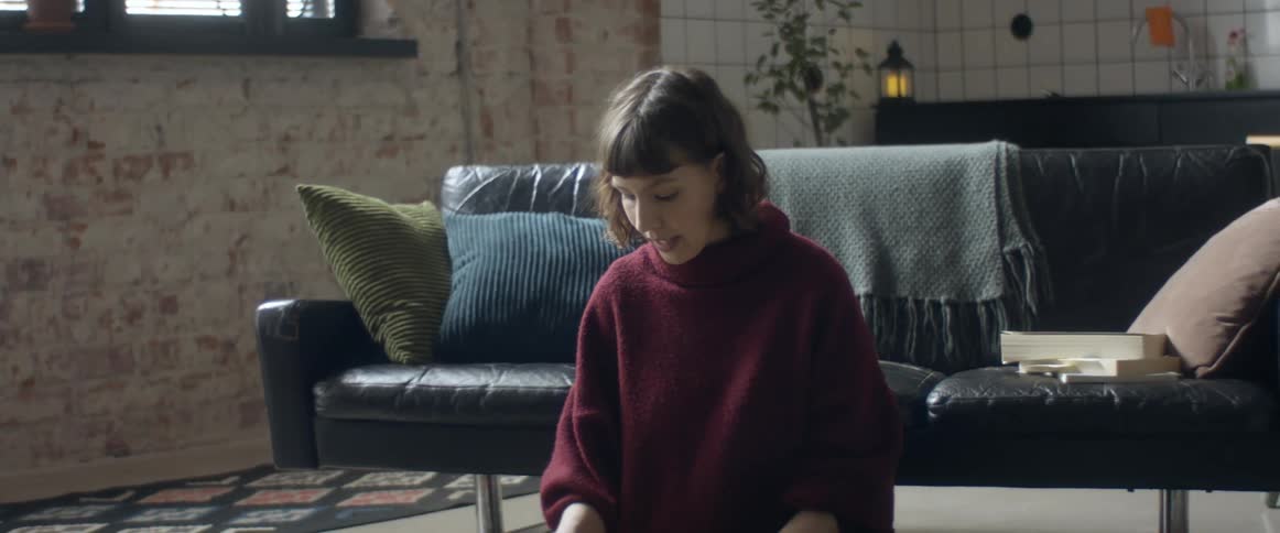 A woman sits on the floor of a home living room while speaking