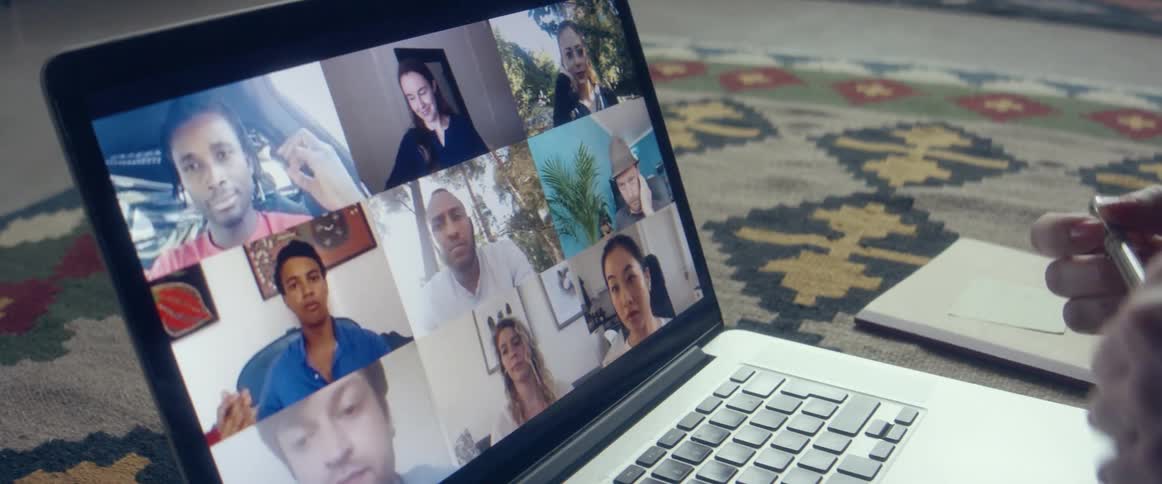 Woman sitting over a rug in the living room talking to a group of friends through a video call on a laptop