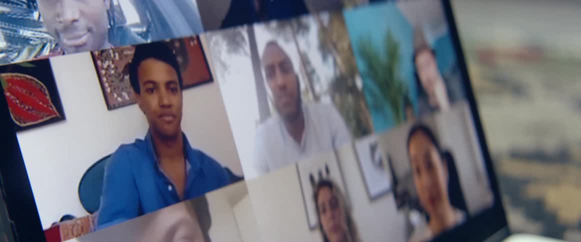 A laptop screen shows a grid of several people participating in a video meeting