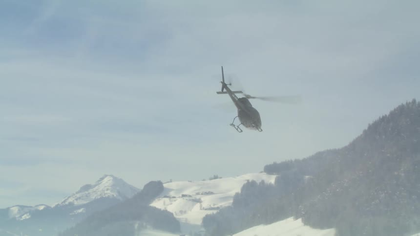 A helicopter flies near snow covered mountains on a cloudy day