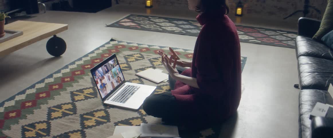 A white female sitting on the floor in a living room talking on a laptop using zoom