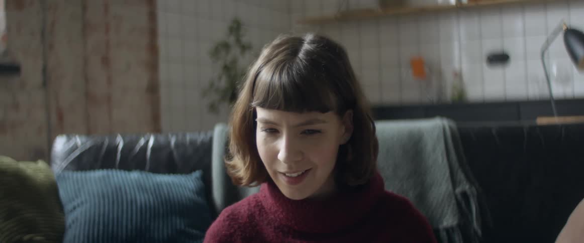 A woman with a sweater in a room with a couch and a wall in the background