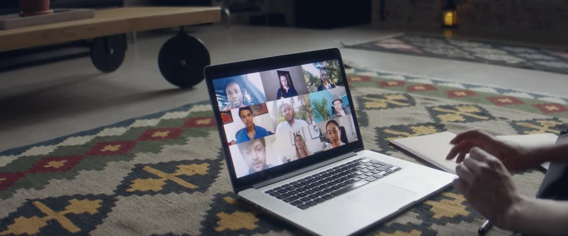 Person participating in video conference via laptop consults notebook
