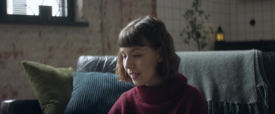 A woman sits in front of a couch talking to someone out of view