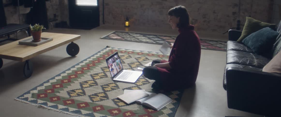 A woman sitting on the floor on a carpet in front of a laptop with a wall and door in the background