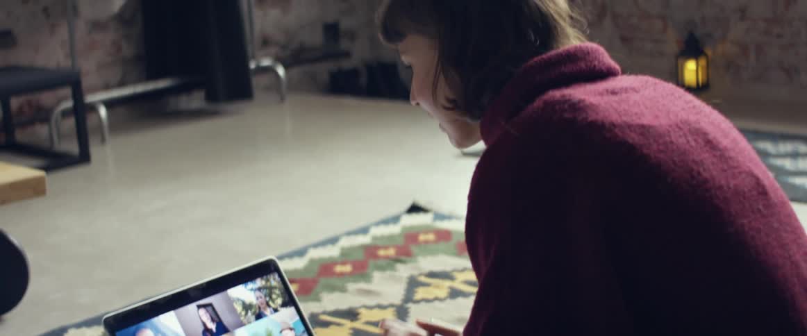 Woman sitting over a rug in the living room talking to a group of friends through a video call on a laptop
