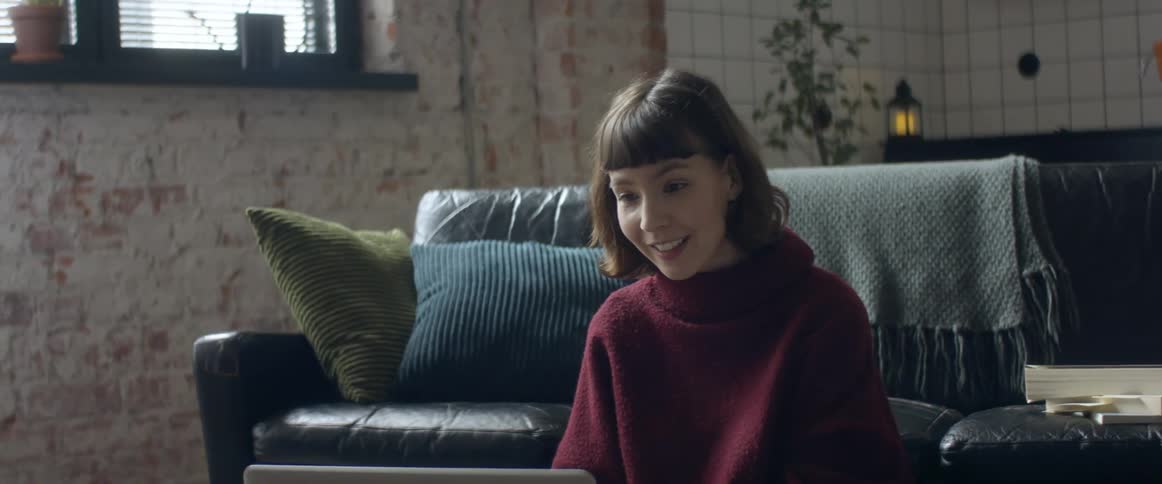 Woman sitting over a rug in the living room talking to a group of friends through a video call on a laptop