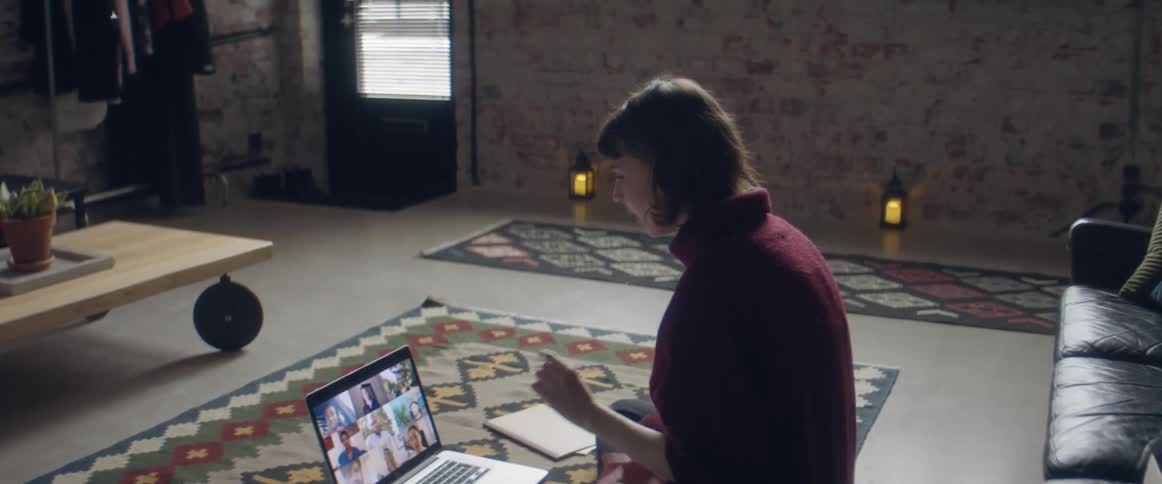 A woman in a room sitting on the floor on a carpet in front of a laptop with a wall and door in the background