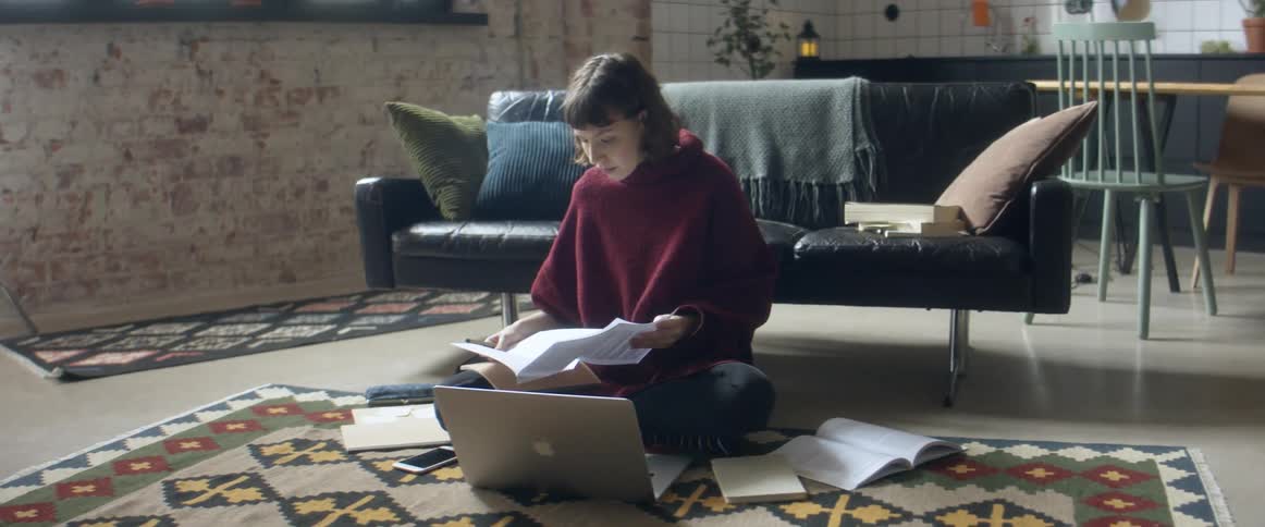 Woman sitting over a rug in the living room talking to a group of friends through a video call on a laptop