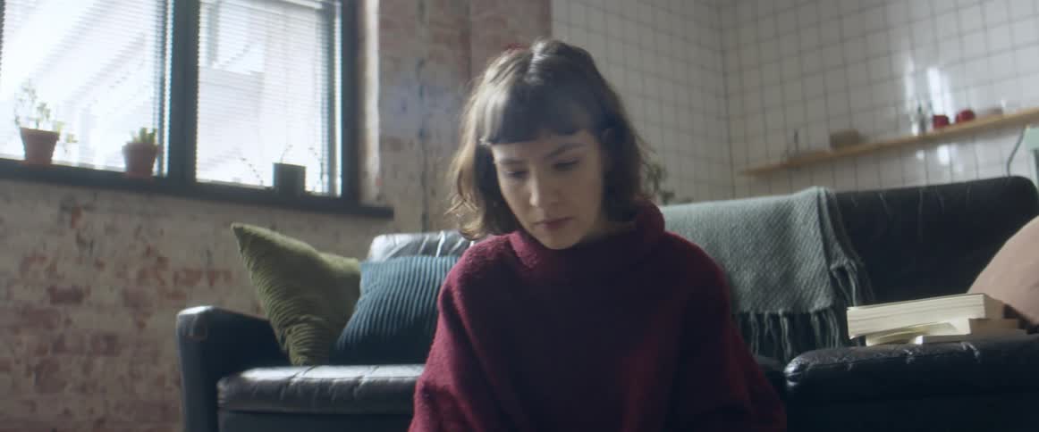 A woman sitting on her apartment floor flips through a notebook while looking at her laptop