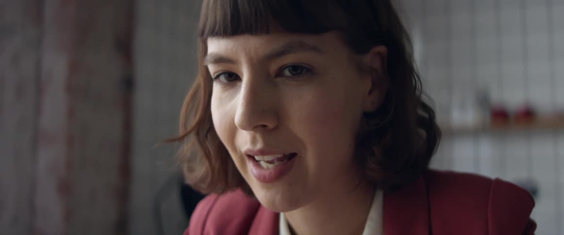 Woman wearing rose colored business jacket talks briefly pursing her lips