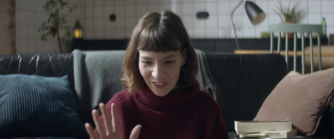 Woman with turtleneck sweater makes a video call and smiles in front of a black couch at home
