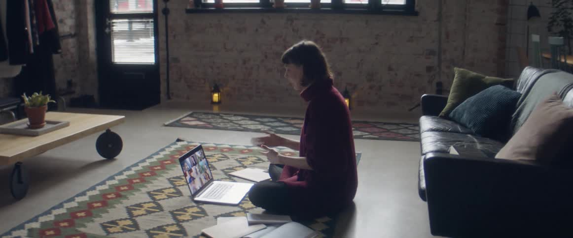 Woman sitting over a rug in the living room talking to a group of friends through a video call on a laptop