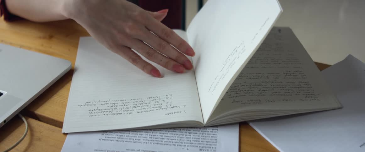 Woman sitting at a desk searching for a note inside a notebook