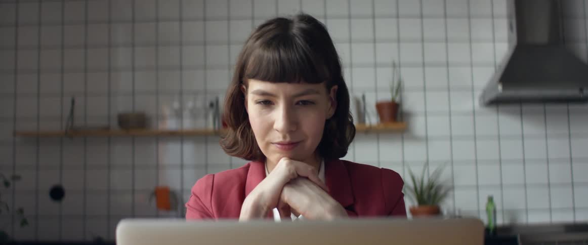 Focused woman working remotely on laptop in modern kitchen