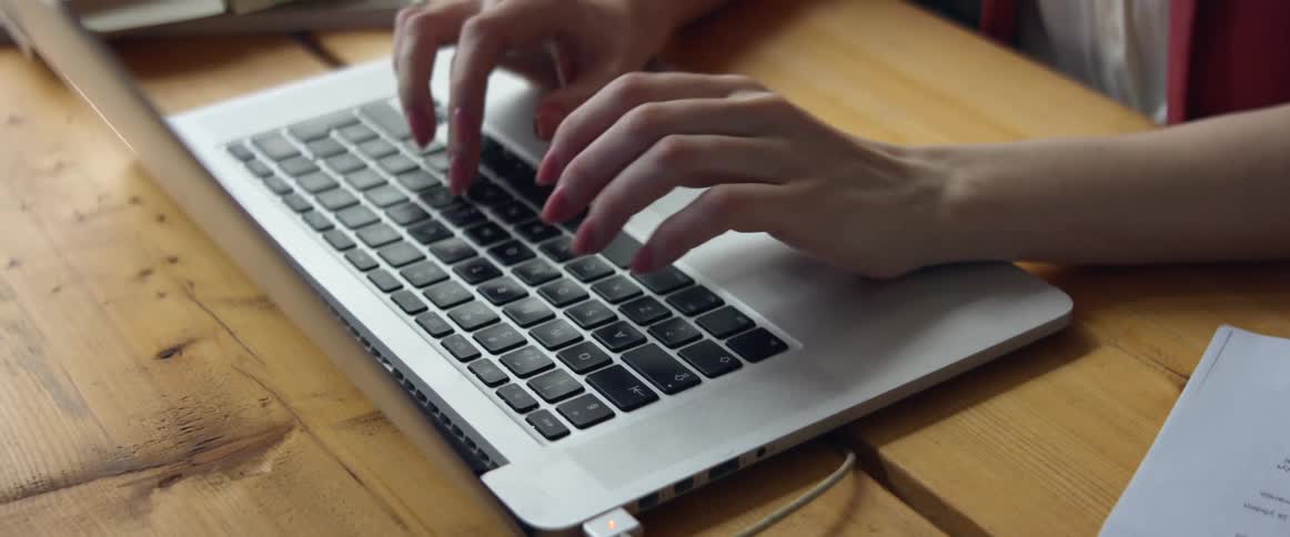 A woman in a room sitting on a chair and typing on a laptop on a desk